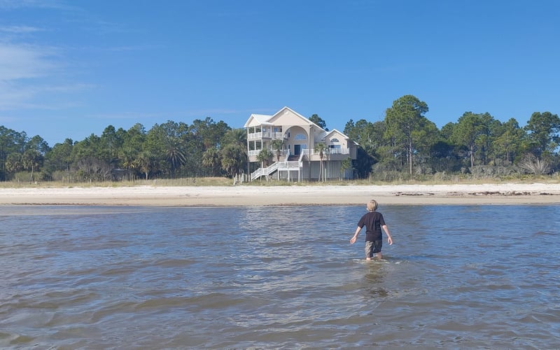 Paradise by the Sea raised beach house at sunset, with palm trees and a paved driveway, on St. George Sound near Carrabelle, Florida